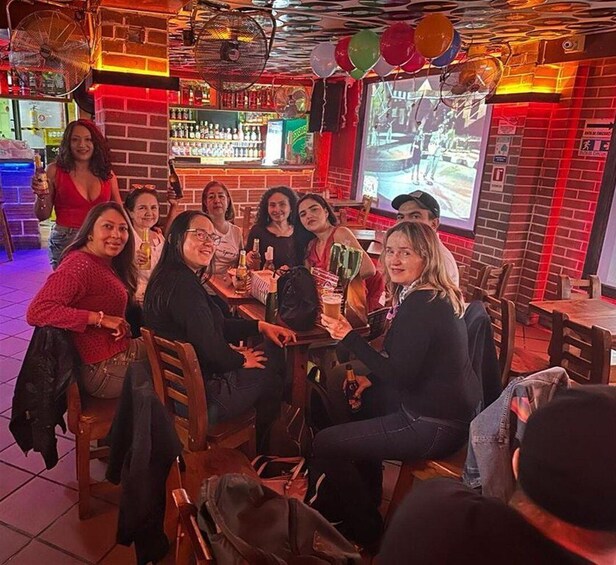 A group of people sitting around a table in a bar with a brick wall and a screen displaying an image. 4