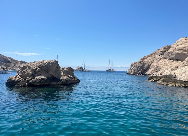 A calm sea with rocky formations and sailboats anchored near the shore. 1