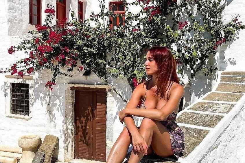 A woman sitting on stone steps in front of a white building with red flowers. 2