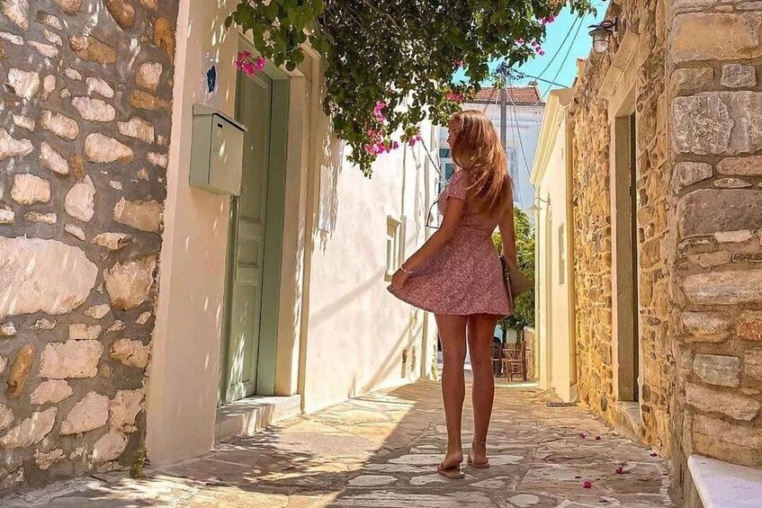 A woman in a pink dress walking down a narrow stone street with buildings on either side. 4