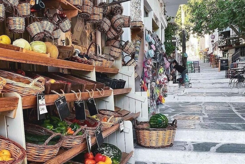 A market with wicker baskets filled with vegetables and fruits, and a street with shops and outdoor seating. 3