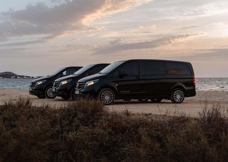 Three black vans parked on a beach with a sunset in the background. 5