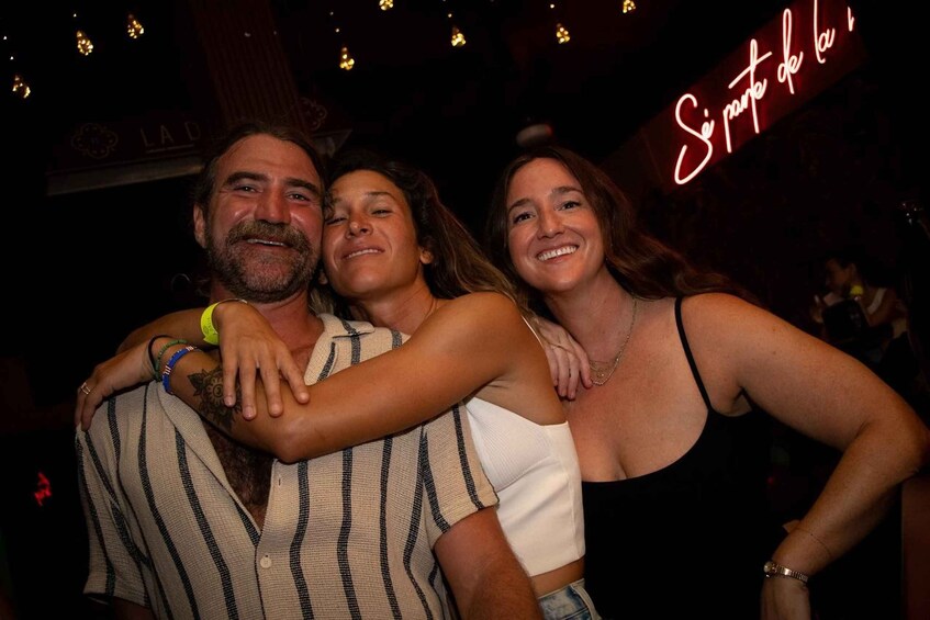A group of people embracing in a dimly lit indoor setting with a neon sign in the background. 3