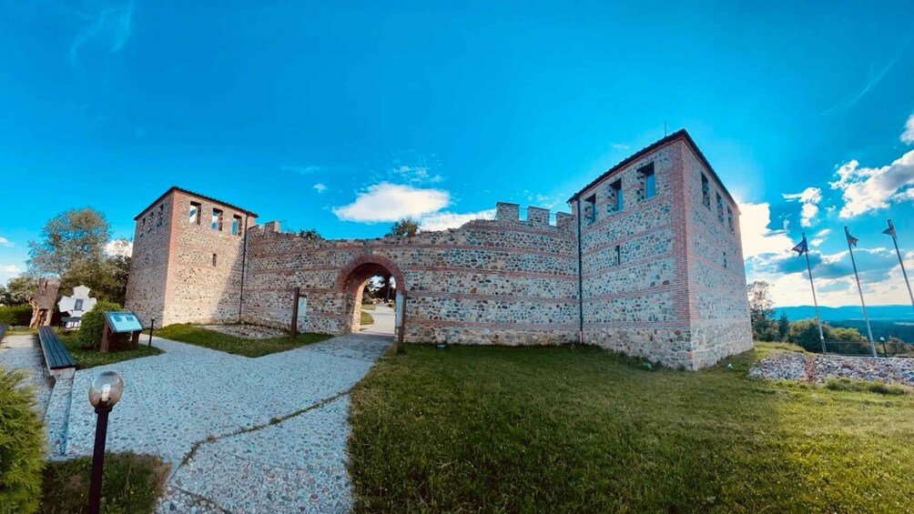 A historic stone building with a large archway, surrounded by a grassy area and a clear blue sky. 5