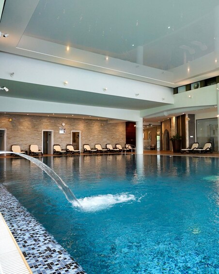 An indoor swimming pool with a water feature, lounge chairs, and a stone wall. 1