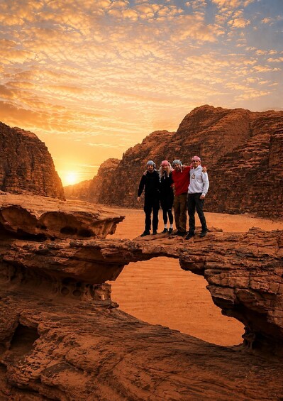 A group of people standing on a rock formation with a sunset in the background. 1