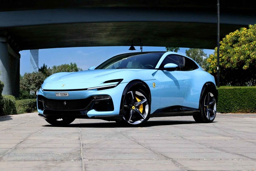 A light blue sports car parked under a bridge. 1