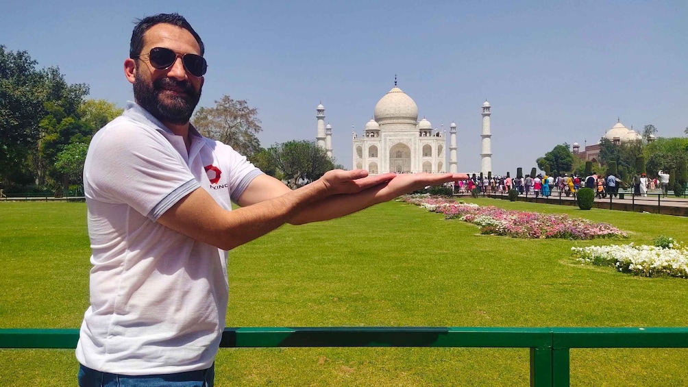 A person standing in front of the Taj Mahal with a hand extended towards the monument. 2