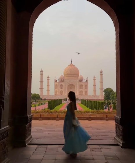A person in a blue dress walking through an archway towards the Taj Mahal. 2