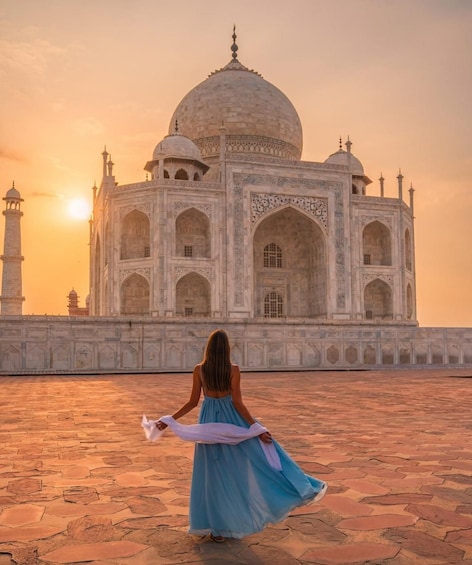 A woman in a blue dress standing in front of the Taj Mahal, with the sun setting in the background. 5