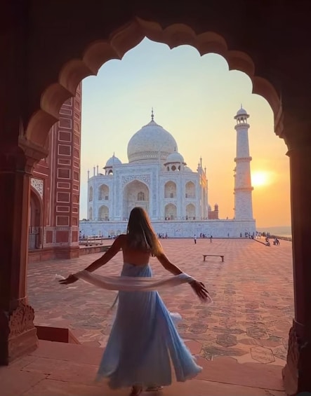 A person in a blue dress standing in an archway, facing the Taj Mahal at sunset. 3