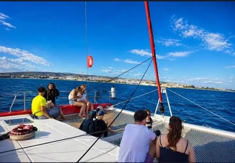 A sailboat with people on deck, a red mast, and a coastline in the background. 3