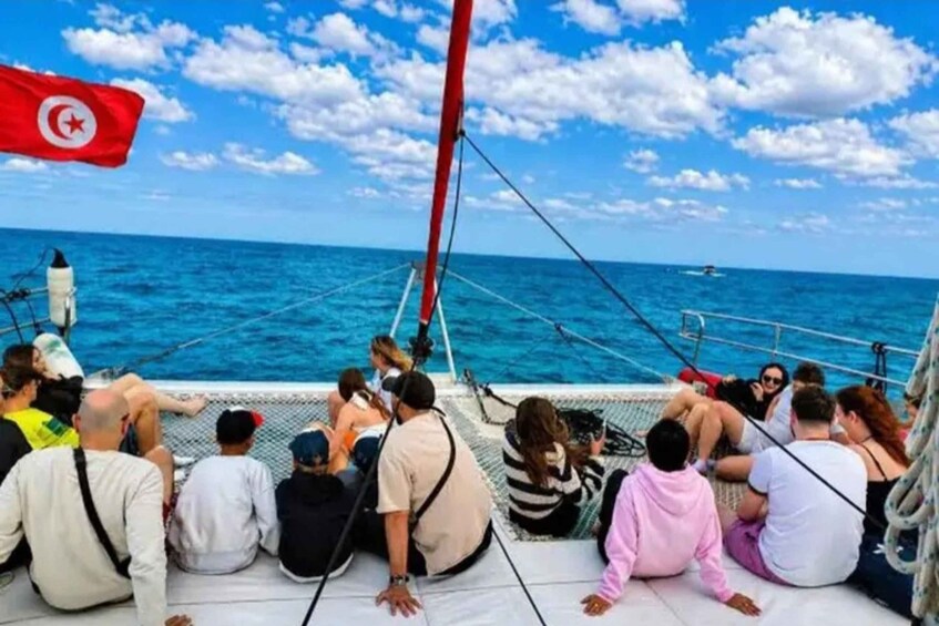A group of people on a boat with a flag, looking out at the sea. 2