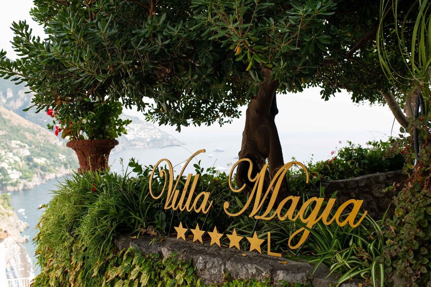 A sign reading "Villa Magia" with a scenic view of a coastal landscape. 2