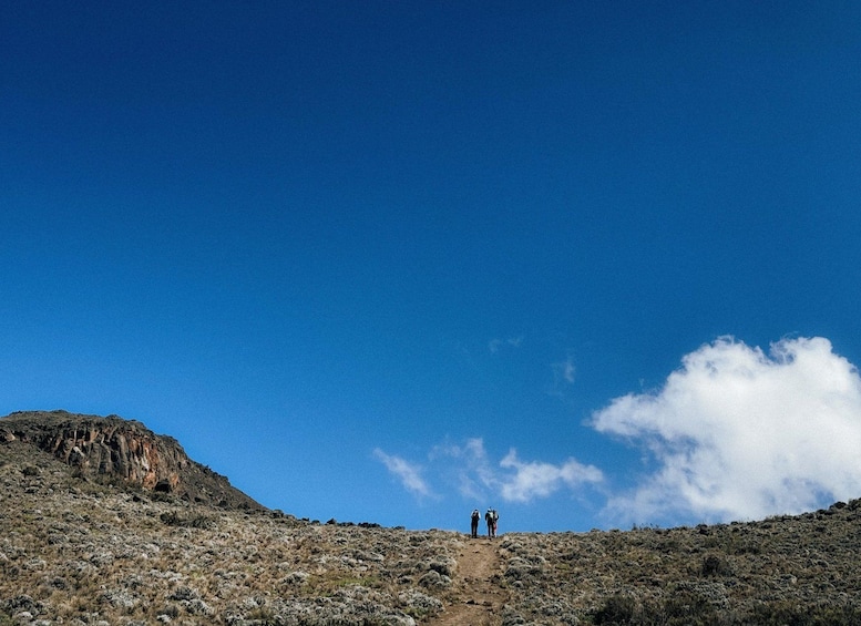 A rocky hill with two hikers at the summit under a clear blue sky. 4