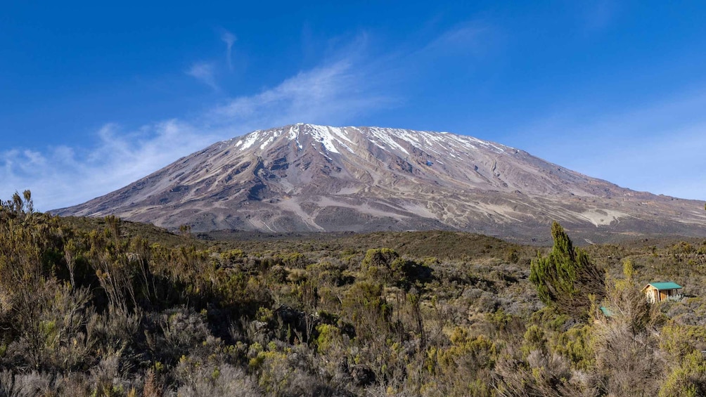 A snow-capped mountain, sparse vegetation, and a small building in the foreground. 3