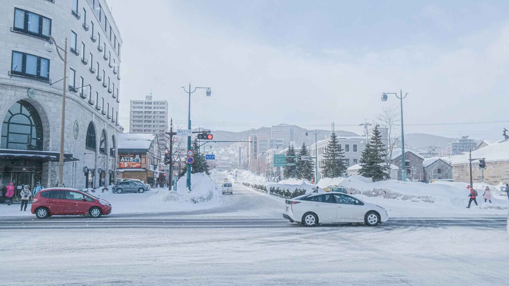A snowy urban street with cars, buildings, and a traffic light. 2