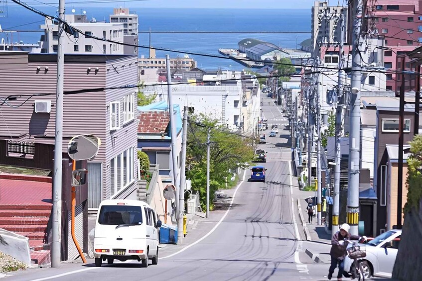 A city street with buildings, a van, a motorcyclist, and a blue bus in the distance. 1