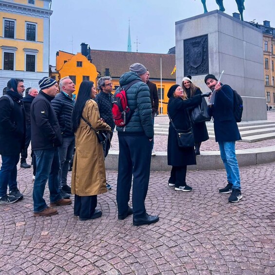 Ryhmä ihmisiä seisoo mukulakivikatua reunustavan muistomerkin edessä. 5