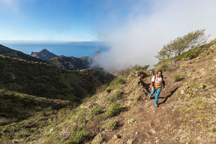A hiker on a mountain trail with a view of the ocean and clouds. 5