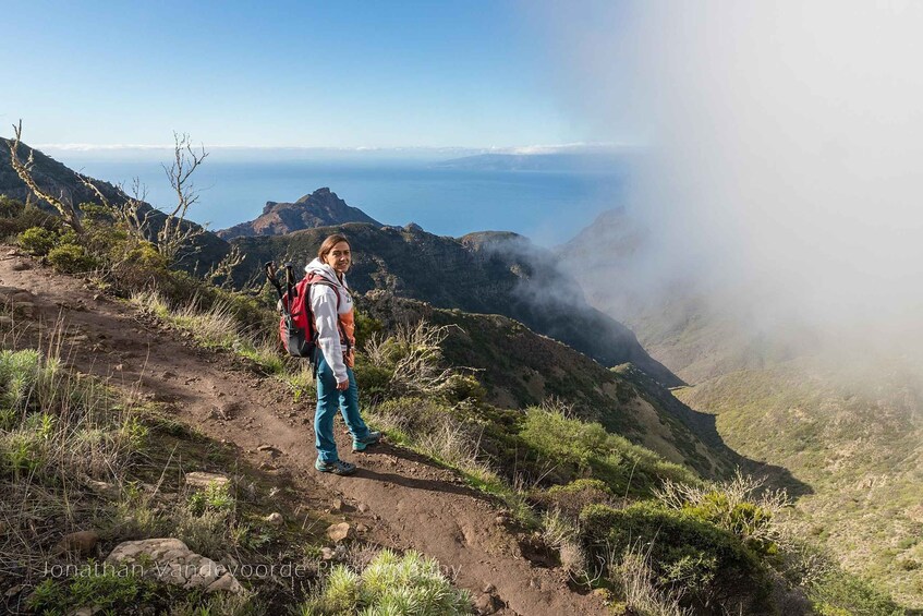 A hiker on a mountain trail with a backpack, surrounded by greenery and a view of the ocean. 4