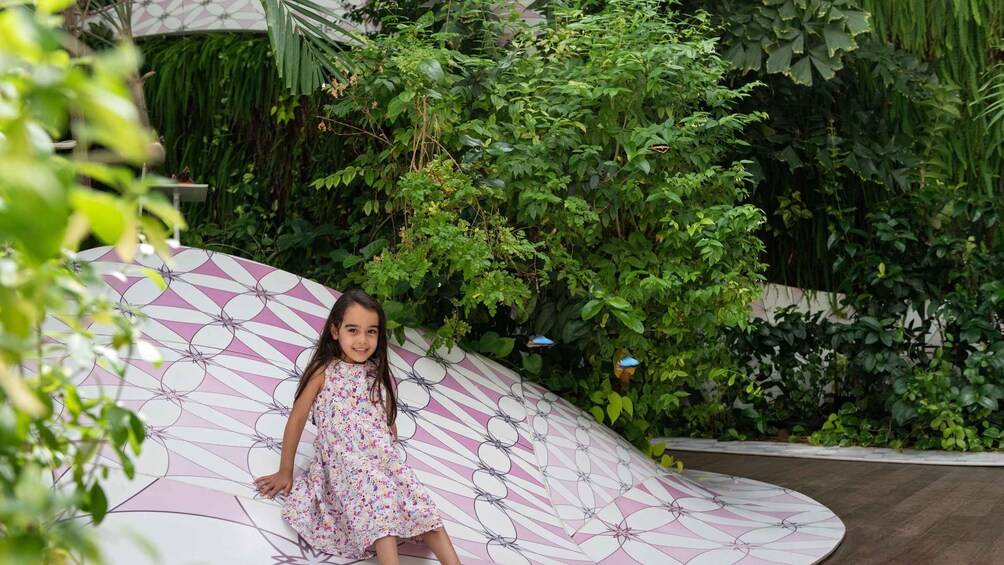 A child on a curved slide with a geometric pattern, surrounded by lush greenery. 2