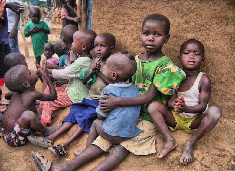 Children sitting on a dirt ground, some holding hands. 2