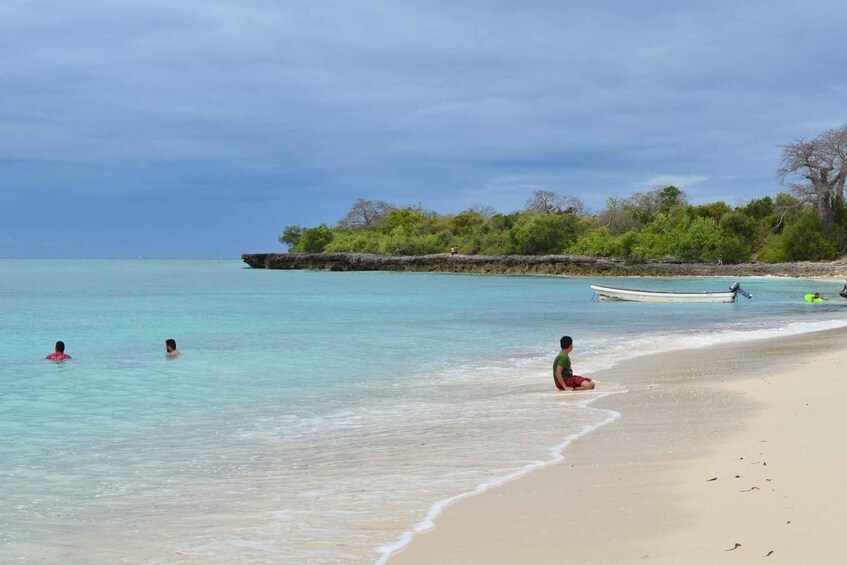 A beach with clear turquoise water, a sandy shore, and a rocky outcrop with trees. 4