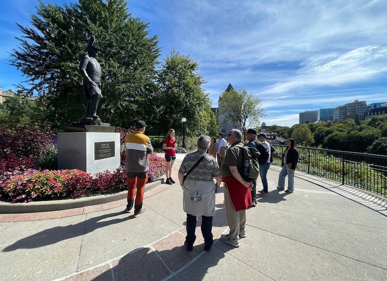 A statue of a man in uniform, a group of people standing on a paved area, and a cityscape in the background. 5