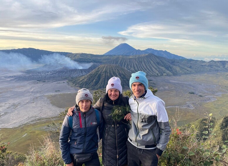 Three people standing on a hill with a mountain in the background. 1