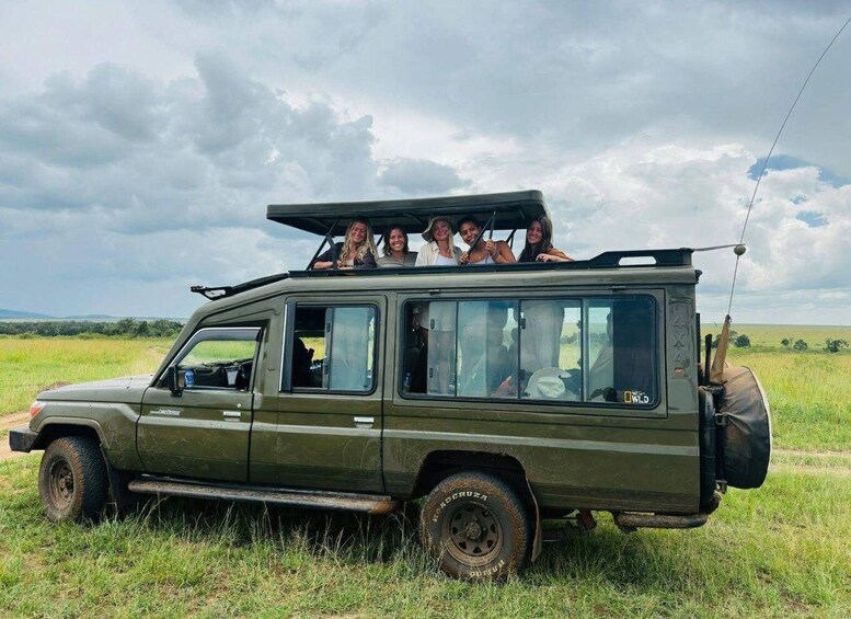 A safari vehicle with passengers on the roof, parked in a grassy field. 2