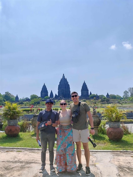 Three people standing in front of ancient temple ruins with a clear sky. 1