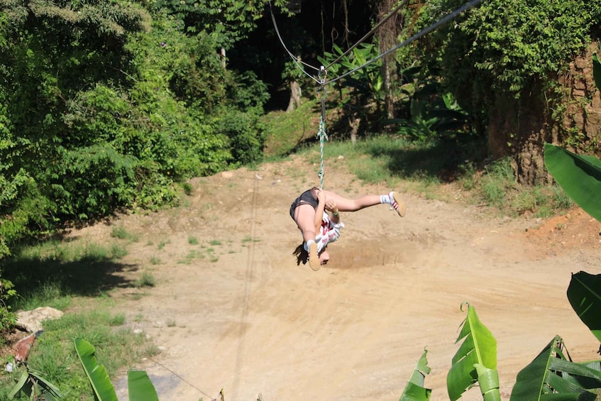 A person swinging on a rope in a natural setting with dense foliage and a dirt path. 5