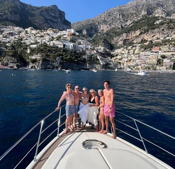 A group of people on a boat with a coastal town and mountains in the background. 2