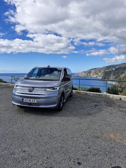 A silver Volkswagen car parked on a gravel road with a scenic coastal view in the background. 1