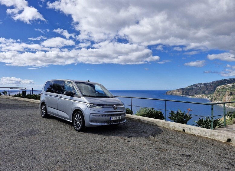 A silver Volkswagen car parked on a coastal road with a scenic view of the ocean and cliffs. 5