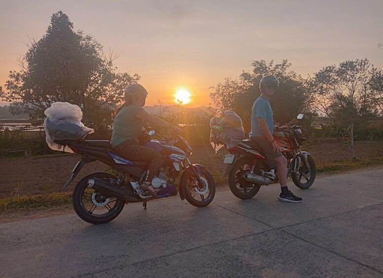 Two motorcycles parked on a road with the sun setting in the background. 2