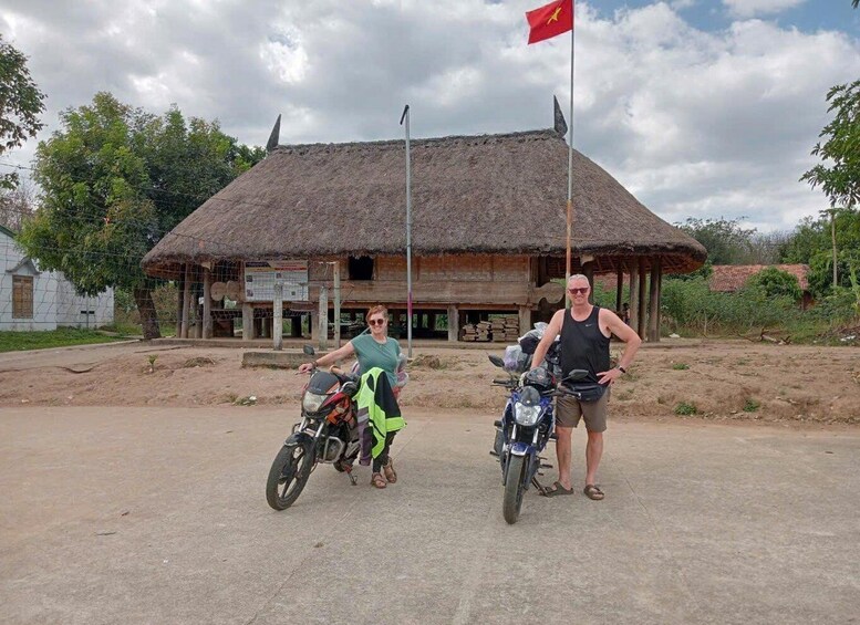 Two motorcycles parked in front of a thatched-roof building with a flag on top. 1