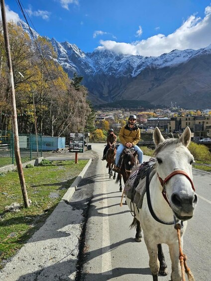 A road with horses and riders, surrounded by mountains and autumn trees. 5