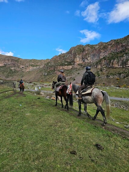 A group of people riding horses along a grassy path with a mountainous backdrop. 2