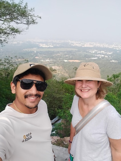Two people standing on a hill overlooking a valley with houses and greenery. 2