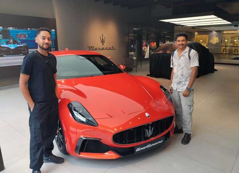 Two men standing beside a red Maserati sports car in a showroom. 1