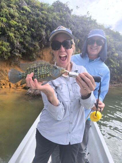 Two people holding a fish in a boat on a river surrounded by greenery. 3