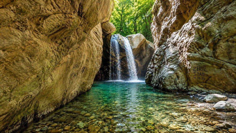 A waterfall in a rocky gorge with clear water and lush greenery. 5