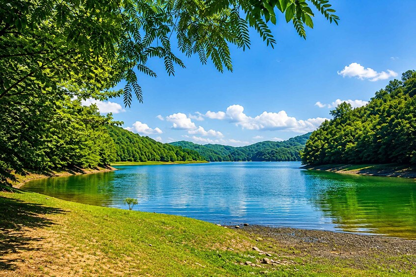 A calm lake surrounded by lush green hills and a clear blue sky. 4