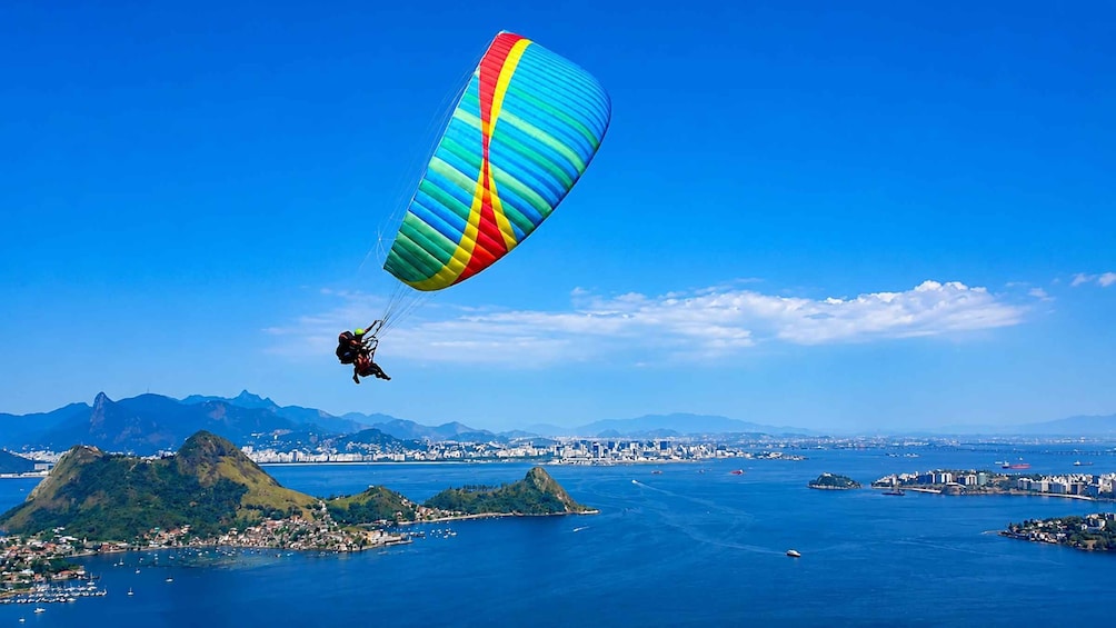 A paraglider flying over a coastal city with mountains in the background. 1