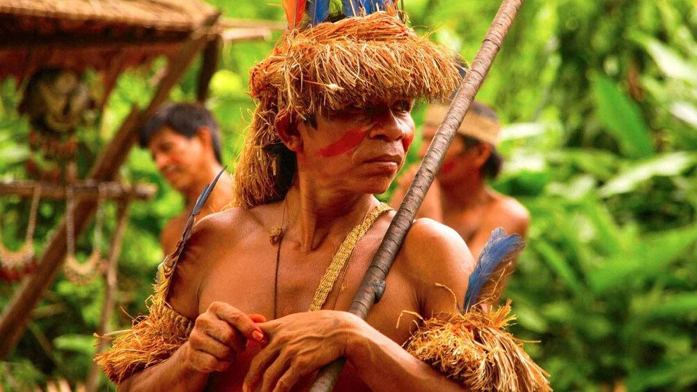 A person in traditional attire with a feathered headdress and a spear. 3