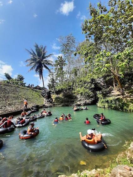 People floating on water in tubes, surrounded by greenery and palm trees. 1