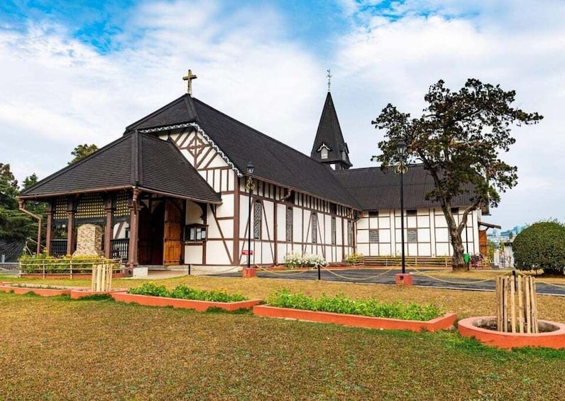 A church with a steeple and a cross on top, surrounded by a garden with a fence. 1