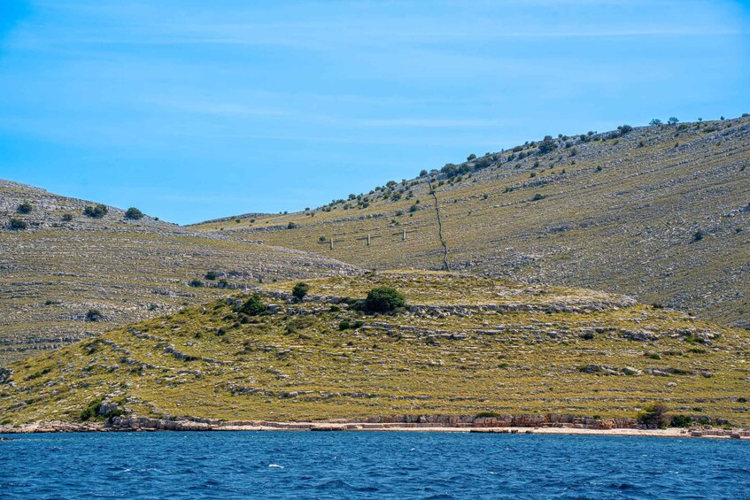 A coastal landscape with a hill, sparse vegetation, and a clear blue sky. 2